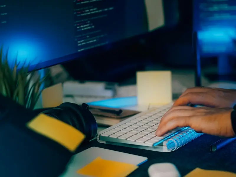 Hands typing at a desk with code on the screens