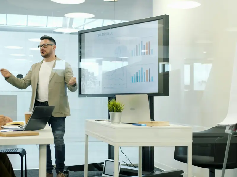 A person presenting charts on a screen in a meeting room